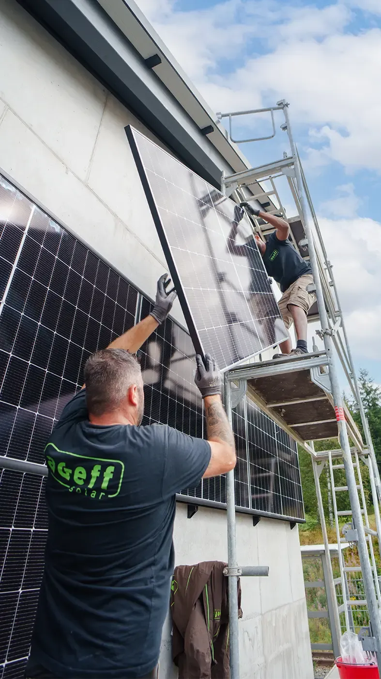 Solartechniker montieren gemeinsam ein Modul an einem Gebäude