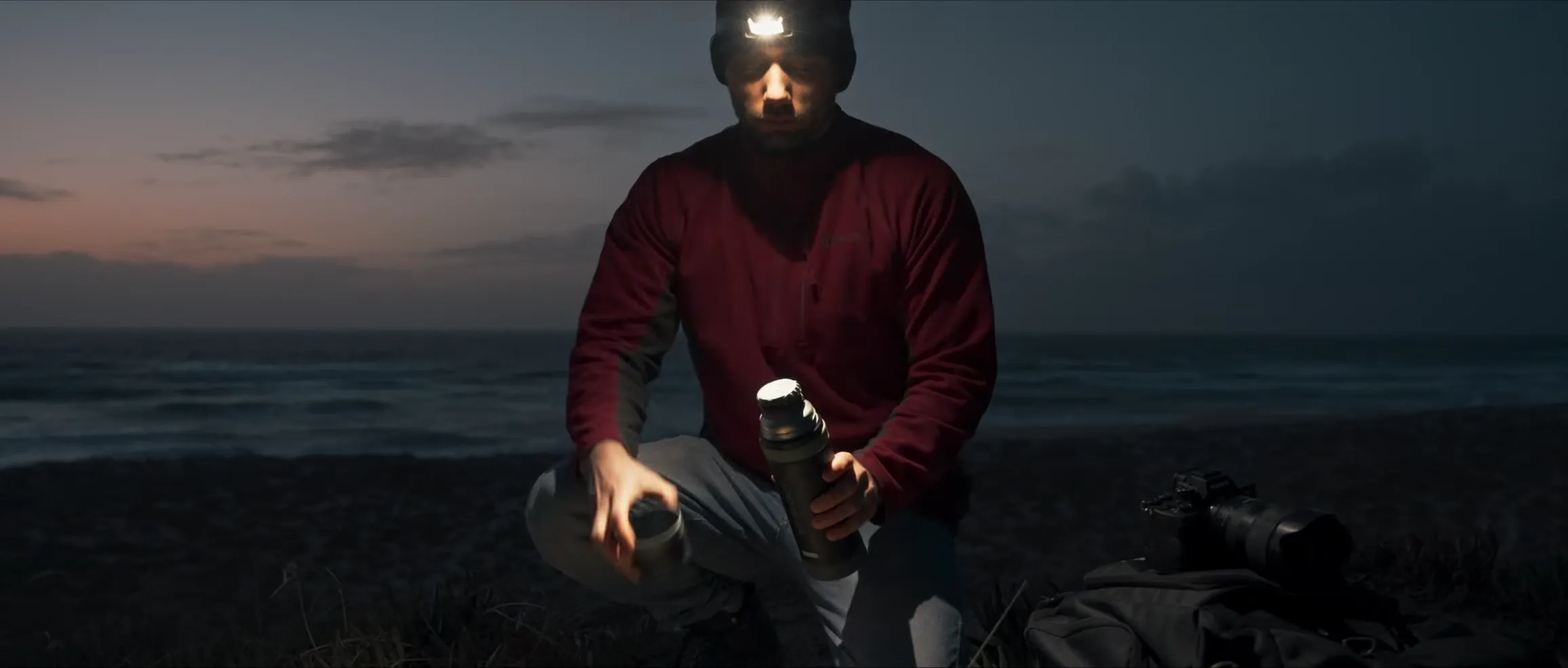 Nachtaufnahme mit Stirnlampe, Thermosflasche und Kamera an der Küste Portugals